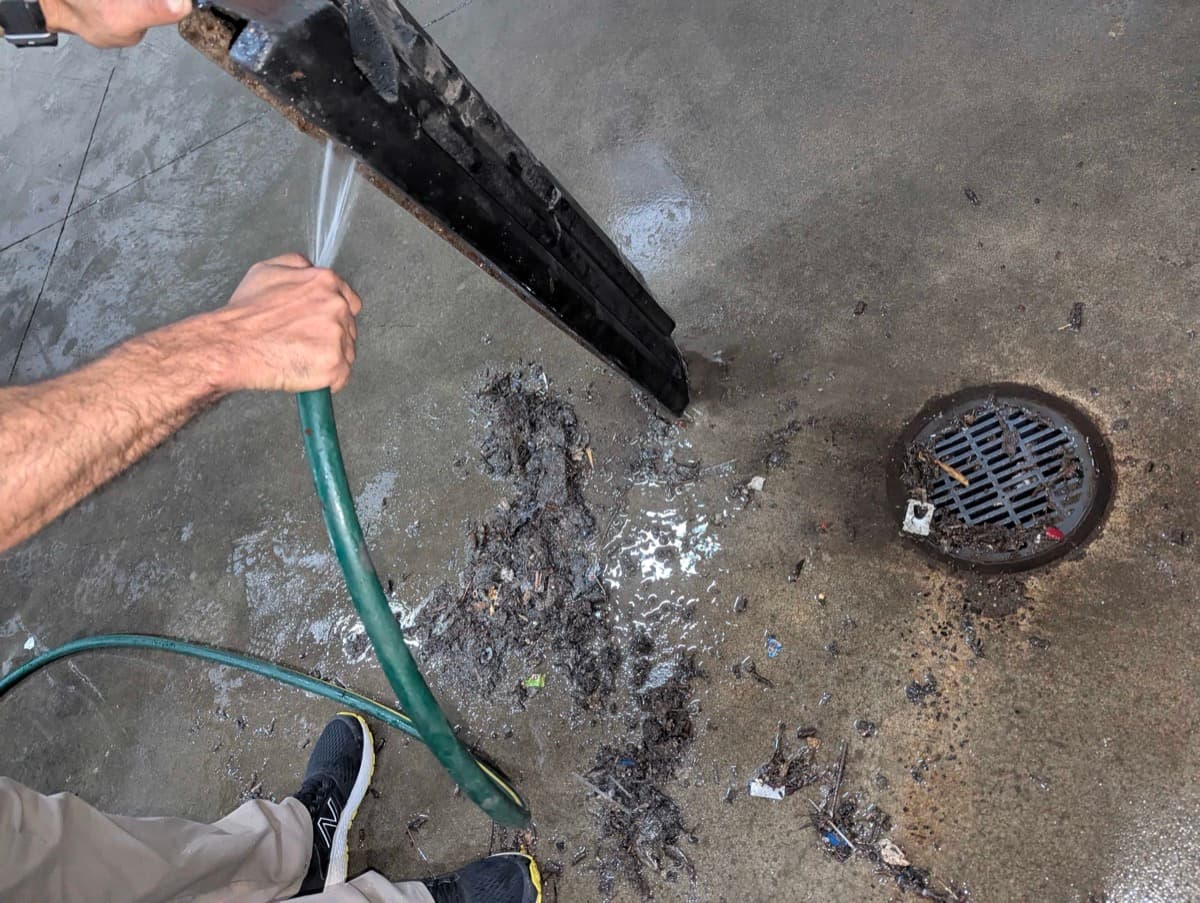 Technician cleaning scrubber squeegee assembly with pressure hose